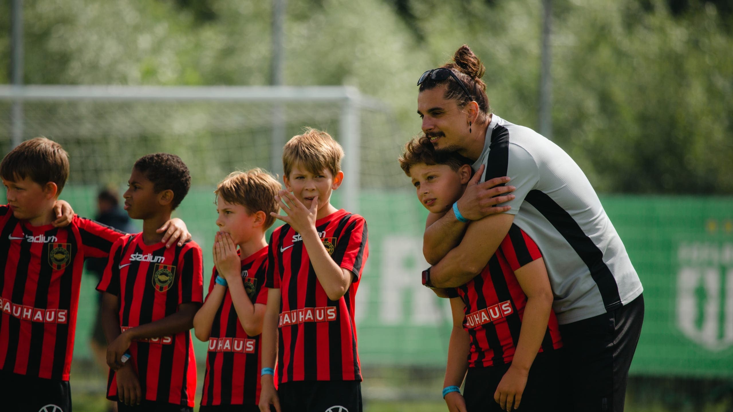 A coach with an arm round a player on the touchline, the rest of the squad watching