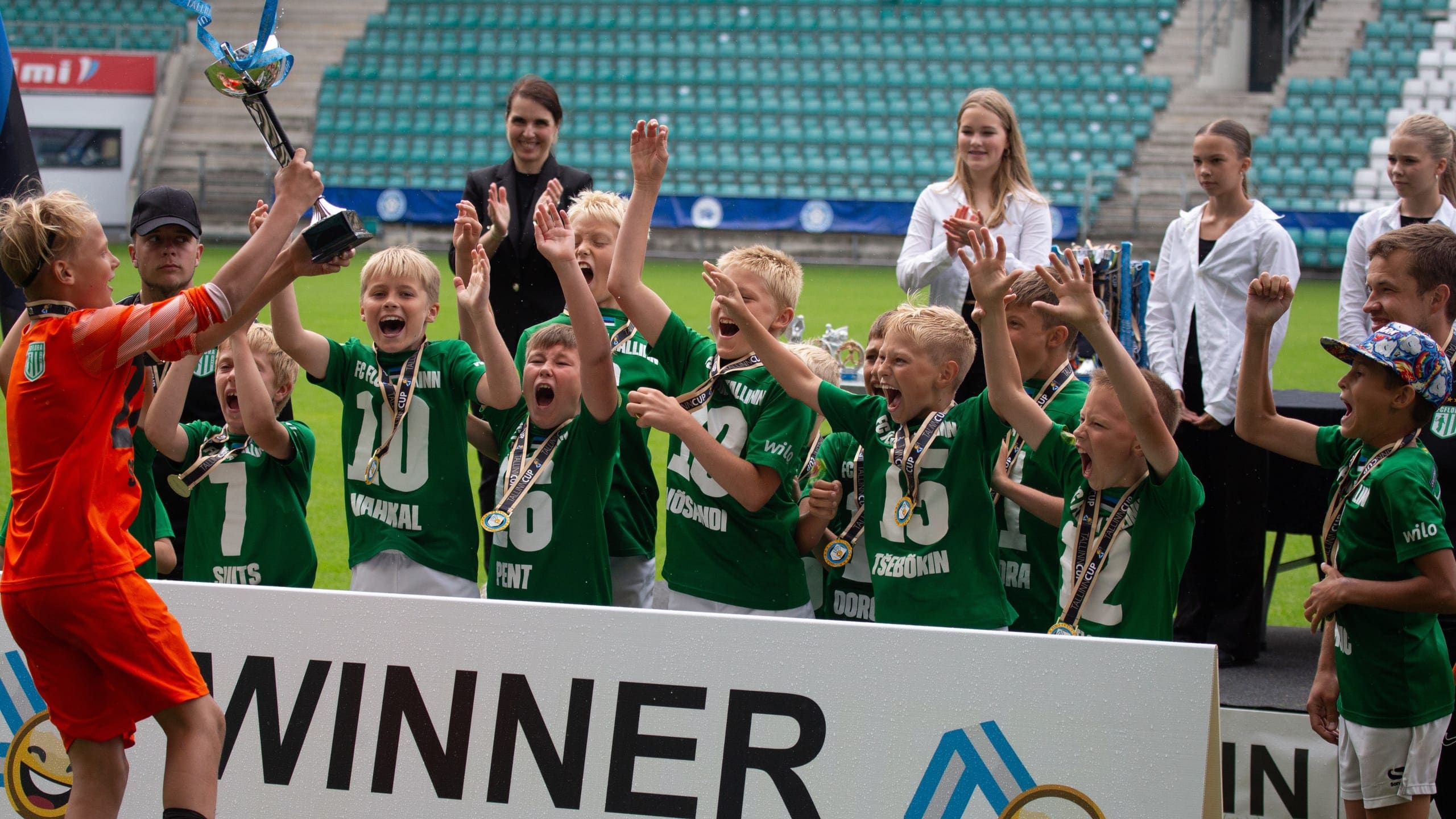 A squad in green lifting the cup on the podium, medals round their necks